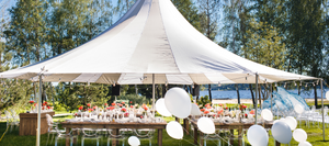 A white party tent setup outdoors on a. clear day surrounded by balloons.