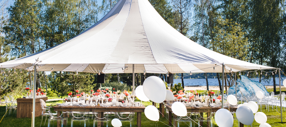 A white party tent setup outdoors on a. clear day surrounded by balloons.